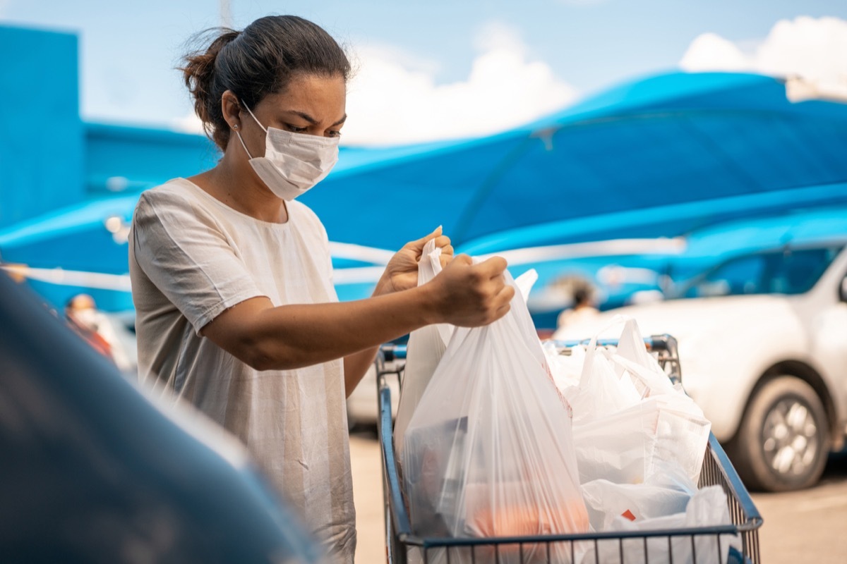 Woman wearing mask putting shopping bags in car trunk