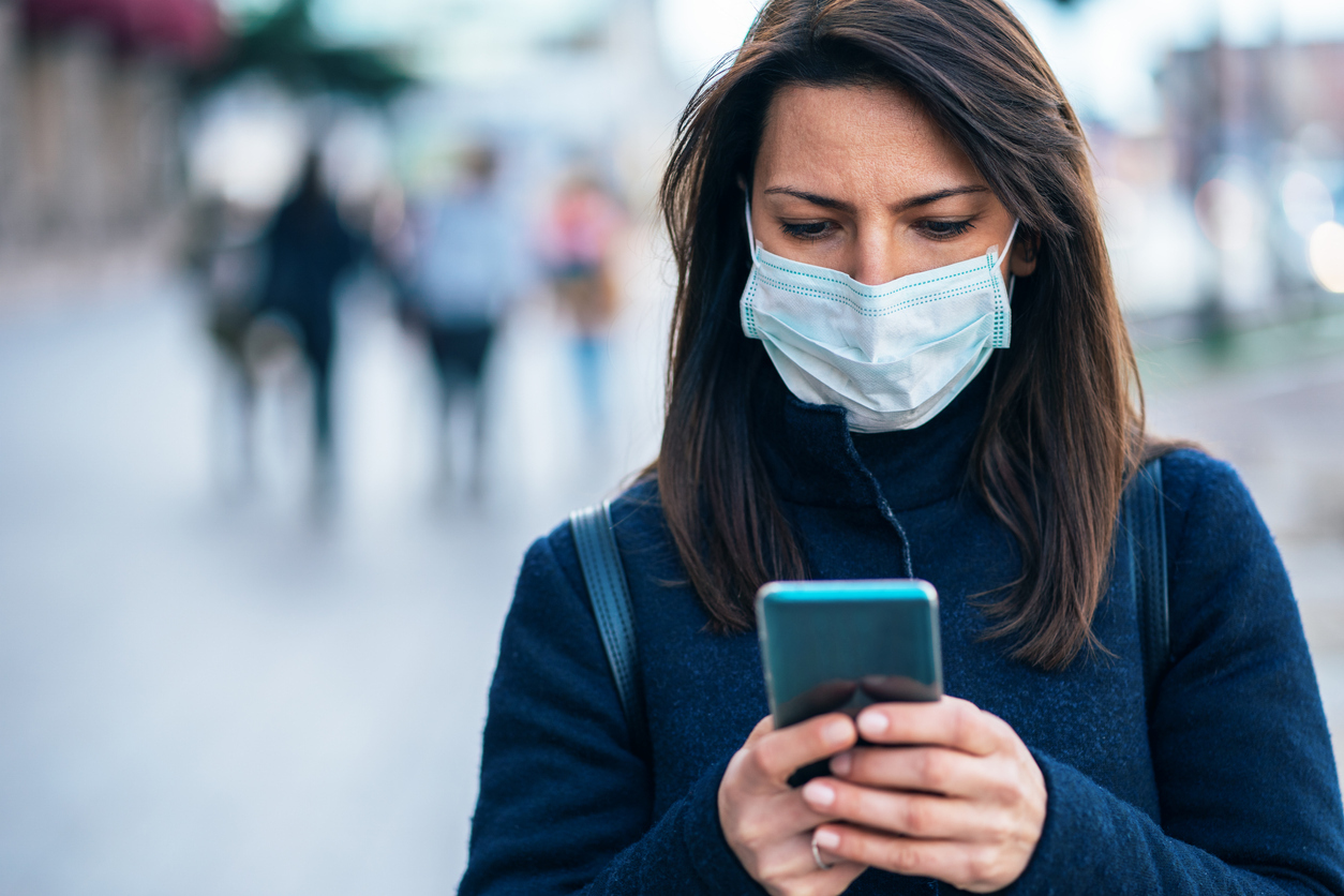 A young woman using her smartphone while wearing a mask due to the coronavirus pandemic.