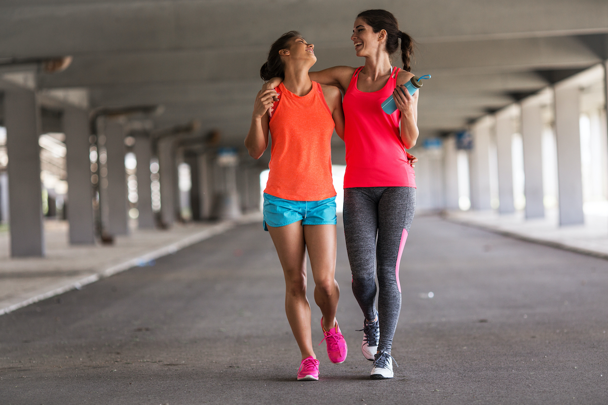 Couple of female friends jogging on the city street under the city road overpass.They relaxing after jogging and making fun.Embracing each other. Walkers