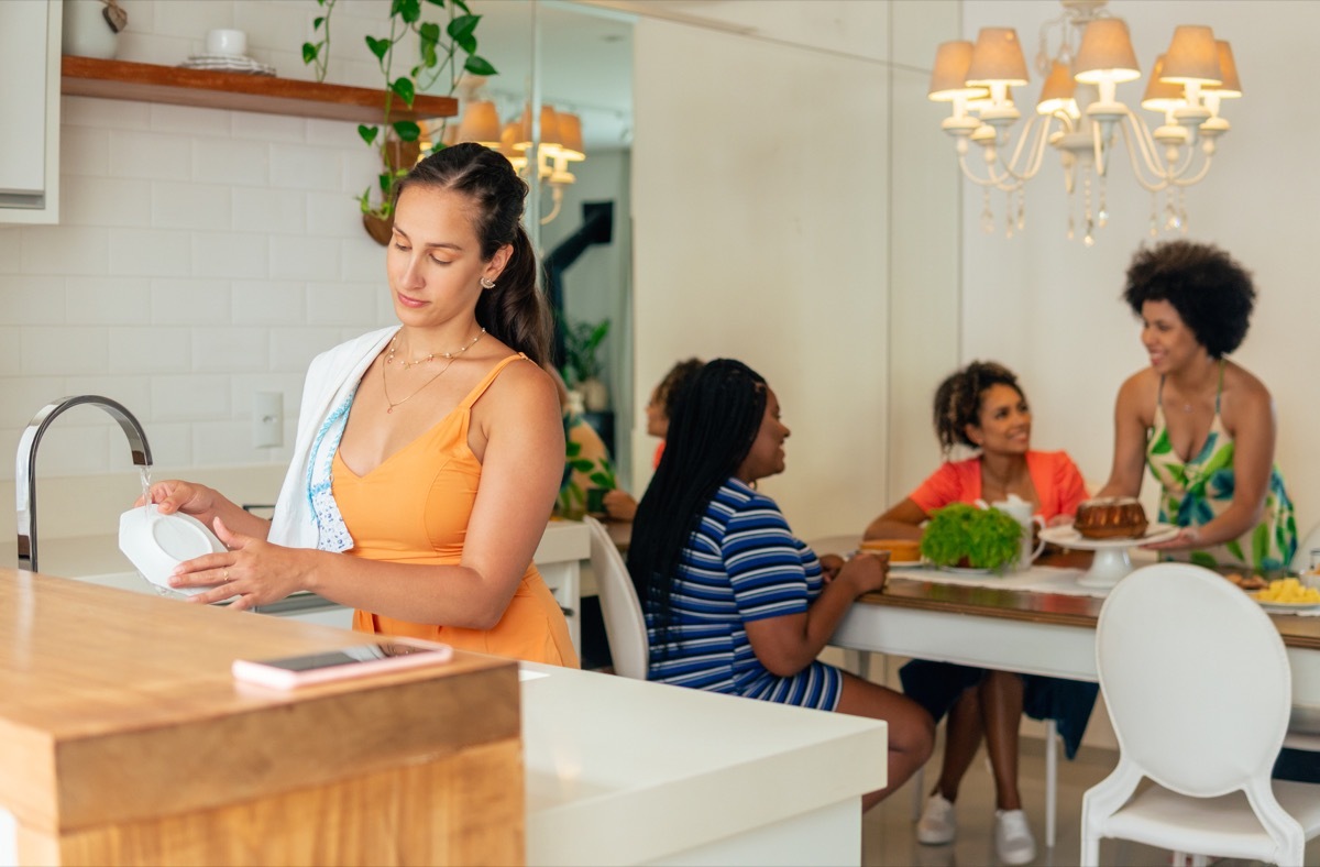 woman washing dish and friends serving food in the kitchen