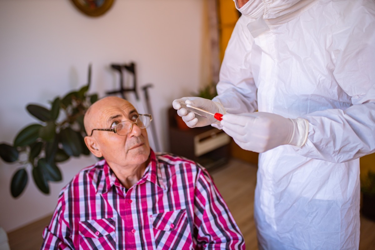 After the doctor in PPE finished with PCR testing, in the nursing home, he talks with a senior patient in the wheelchair explaining to him how to stay safe during the COVID-19 pandemic