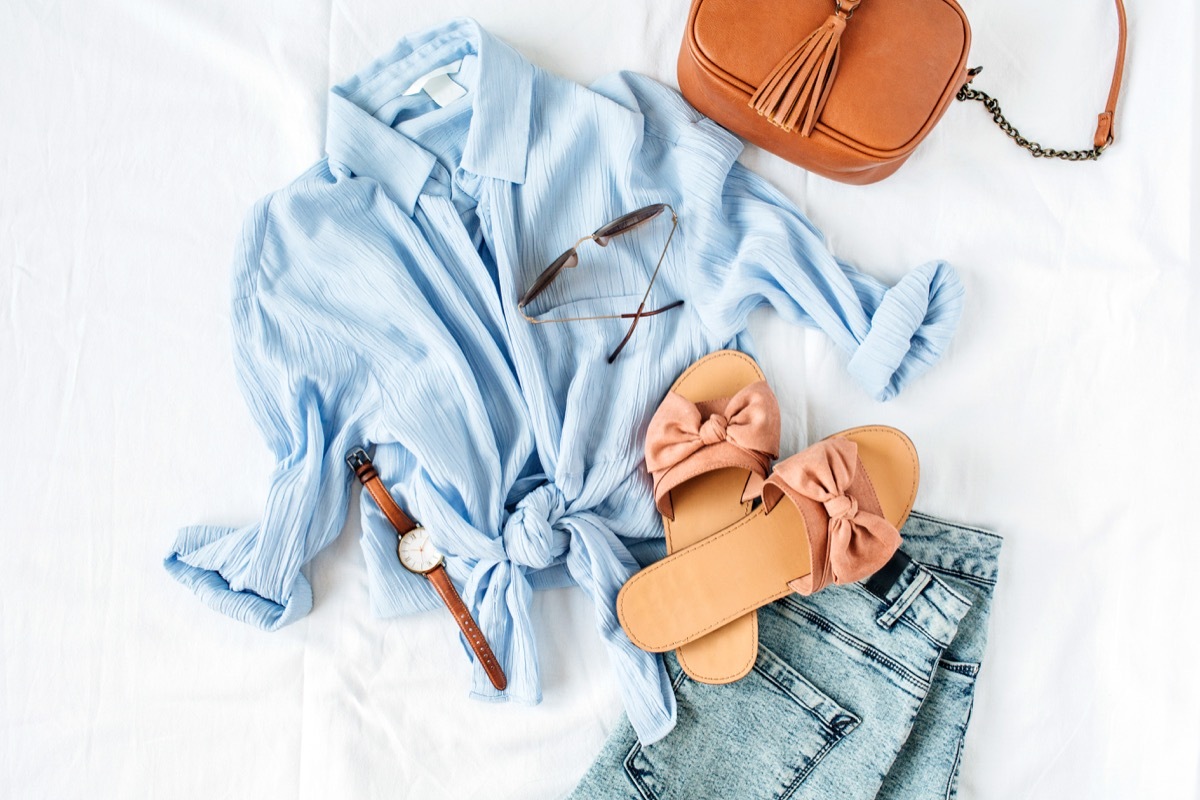 Feminine summer fashion composition with blouse, slippers, purse, sunglasses, watch, jean shorts on white background. Flat lay, top view minimalist clothes collage. Female fashion blog, social media.