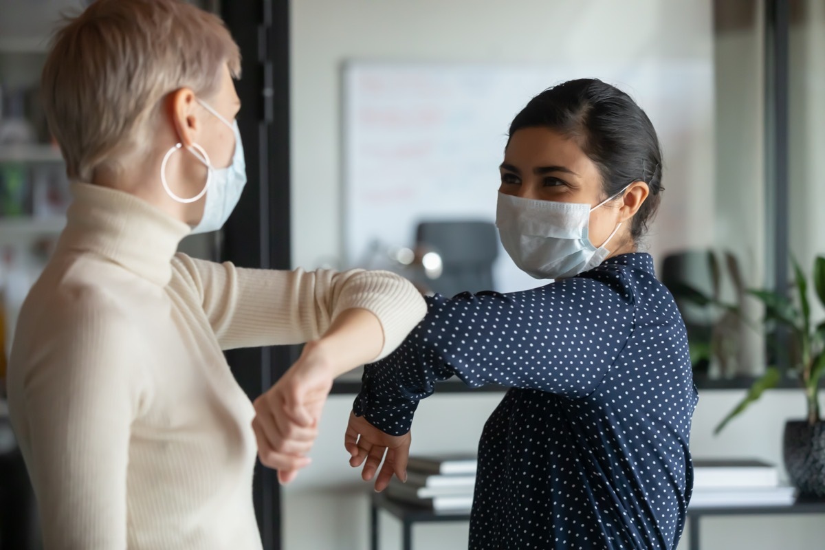 Women with masks on, bumping elbows