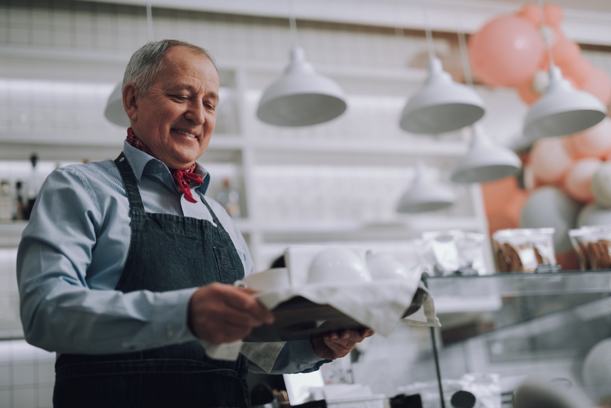 Waist up portrait of male cafe worker looking at hot drink and smiling. He wearing elegant red neckerchief