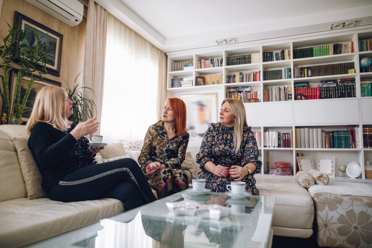 three mature women enjoying their time together at home, drinking coffee.