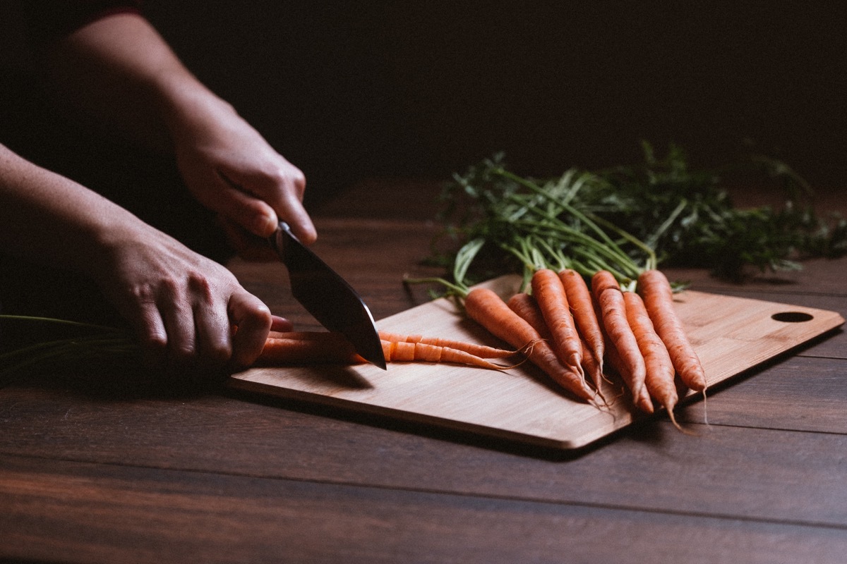 A bunch of fresh raw carrots with stemsWoman cutting carrots and a bunch of fresh raw carrots with stems