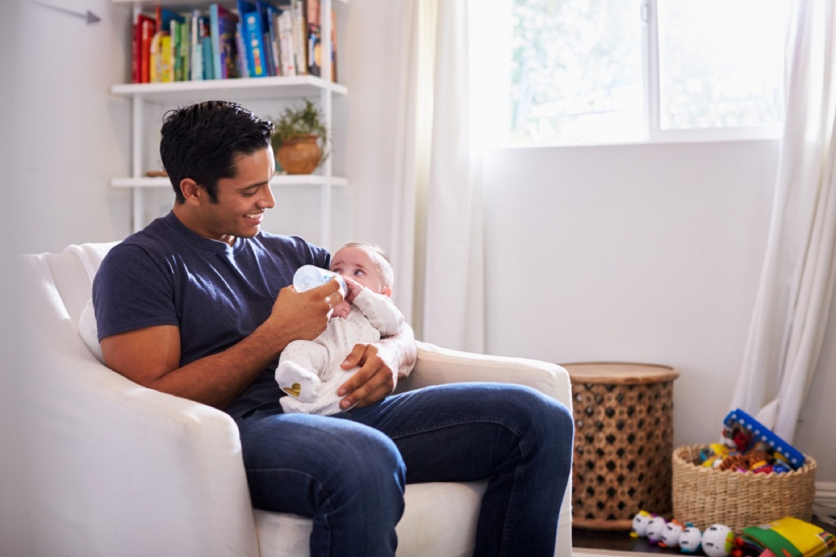 hispanic man holding baby on lap and feeding them with a bottle in a white room