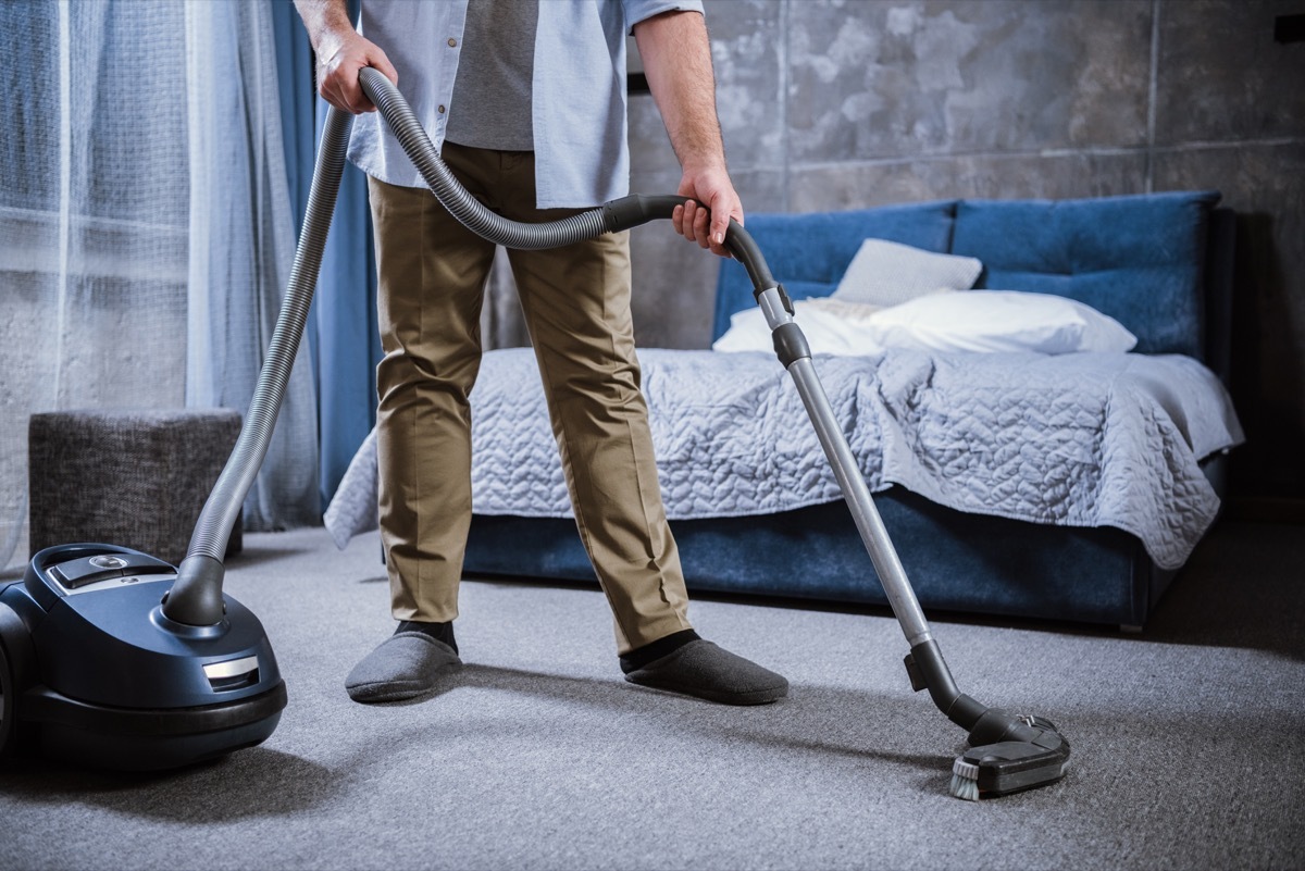 Man vacuuming bedroom carpet