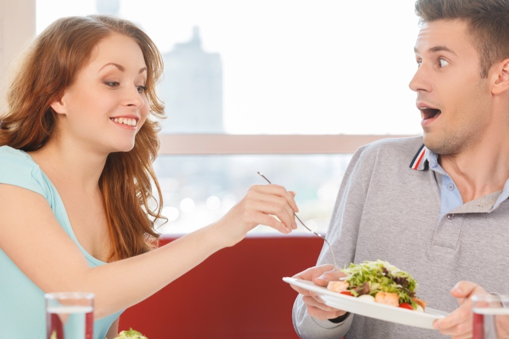 Woman stealing a bite of food from her boyfriend's plate