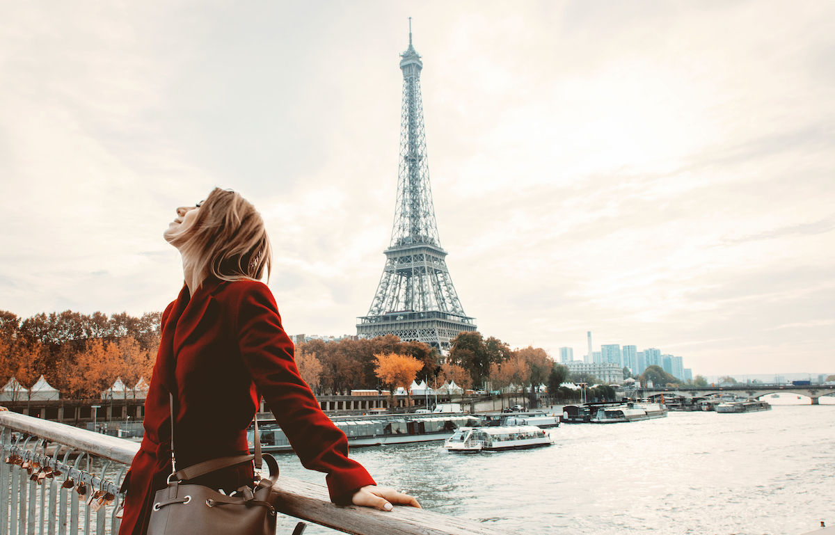 Style redhead girl in red coat and bag at parisian street with view at Eiffel tower in autumn season time