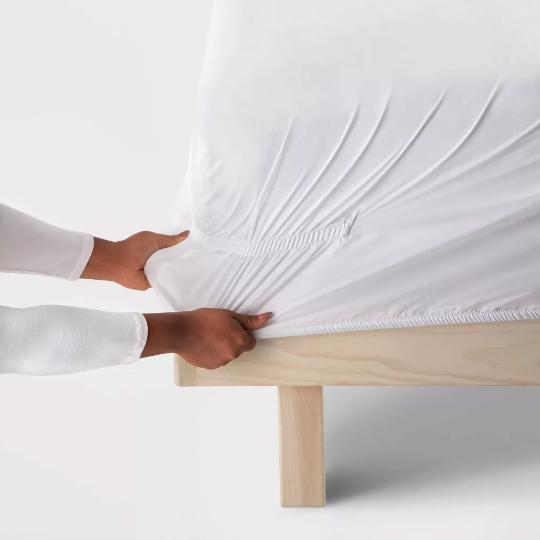 Close up of a woman putting Target's Threshold sheets on a bed