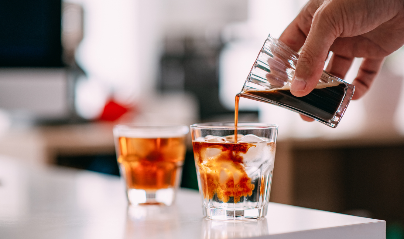 A close up of a person pouring an espresso shot into a glass of tonic