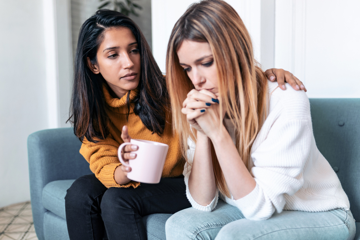 A young woman comforting her sad friend while sitting on the couch.