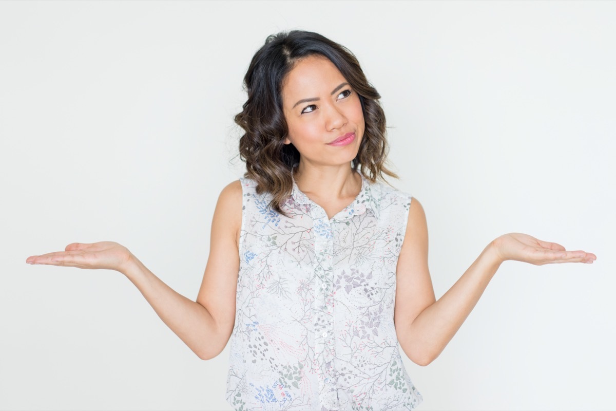 Pensive Asian woman spreading hands.