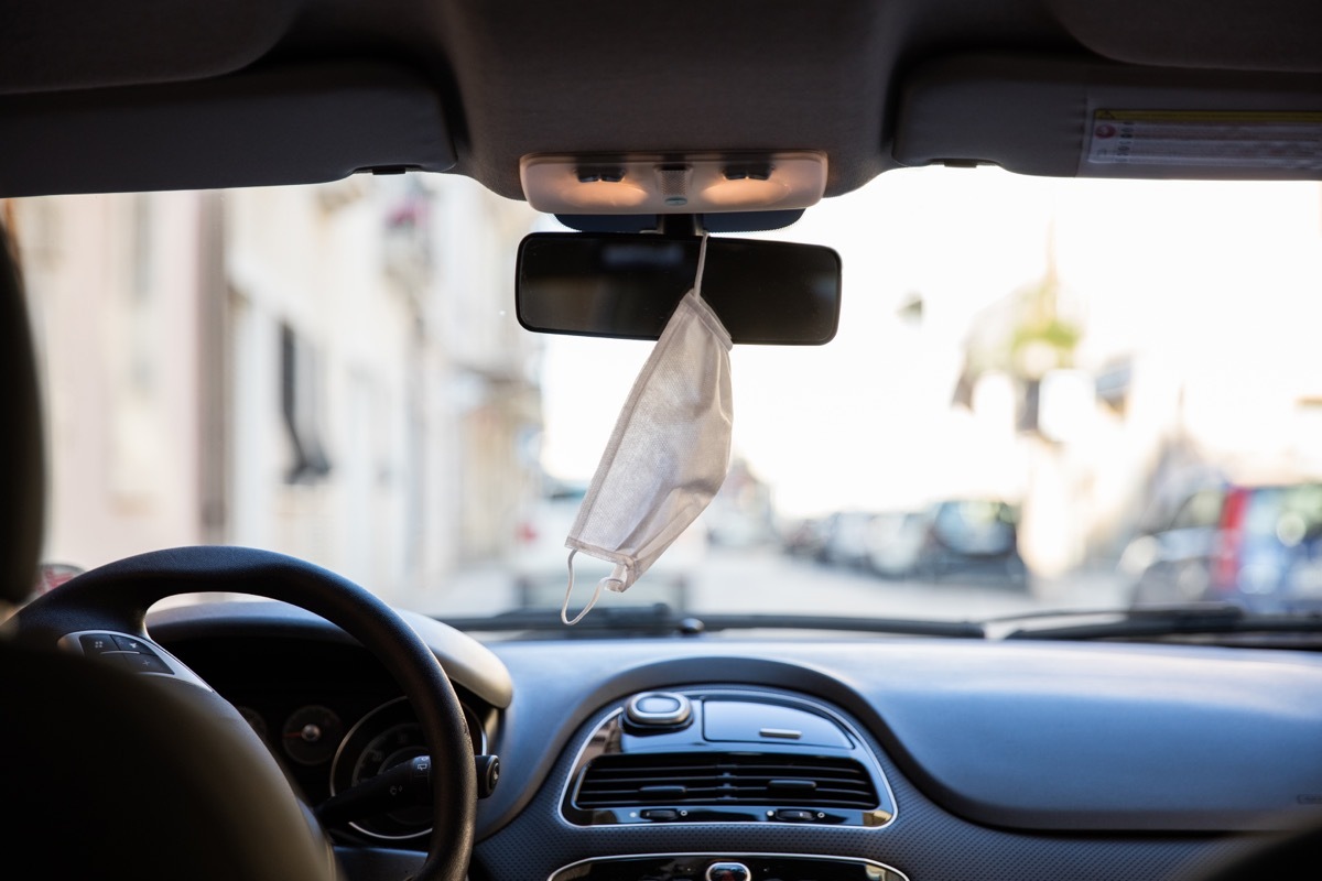 Protective face mask hanging in the car rear-view mirror during Covid-19 pandemic.