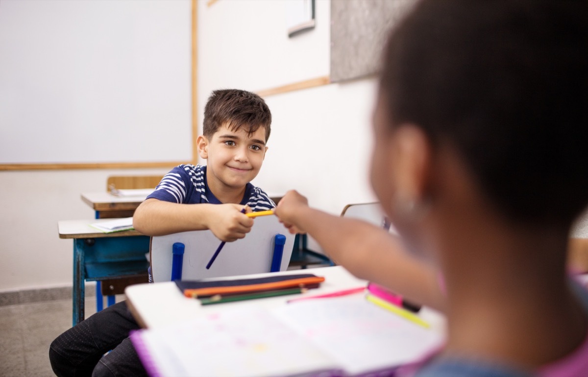 young student handing his pencil to another students in a classroom