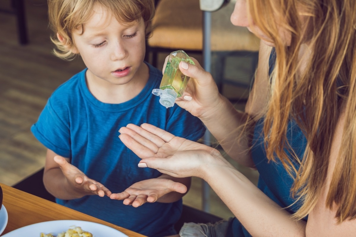 White mother using hand sanitizer on young son