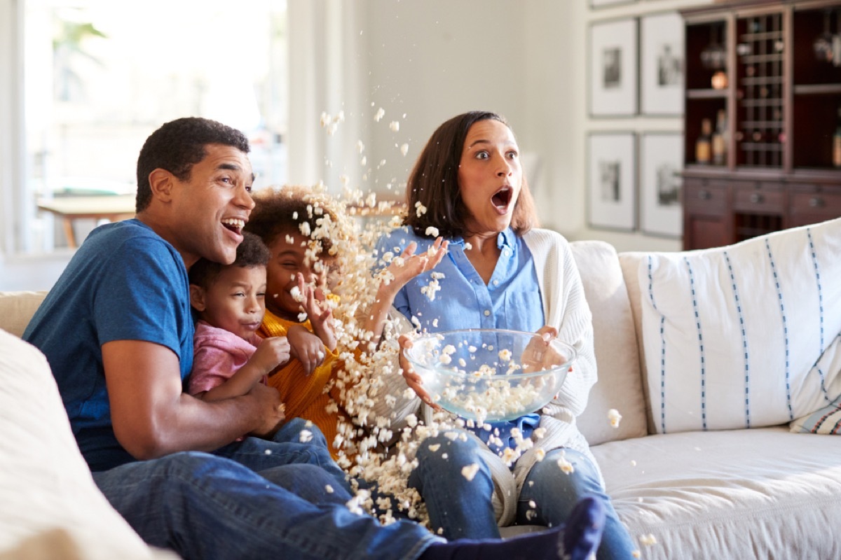 family on the couch watching movie while popcorn spills on the floor, best halloween movies for kids