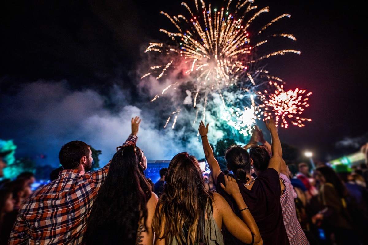 Rear view of crowd of people watching fireworks at night.