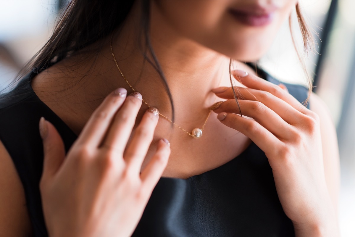 young asian woman putting on pearl necklace