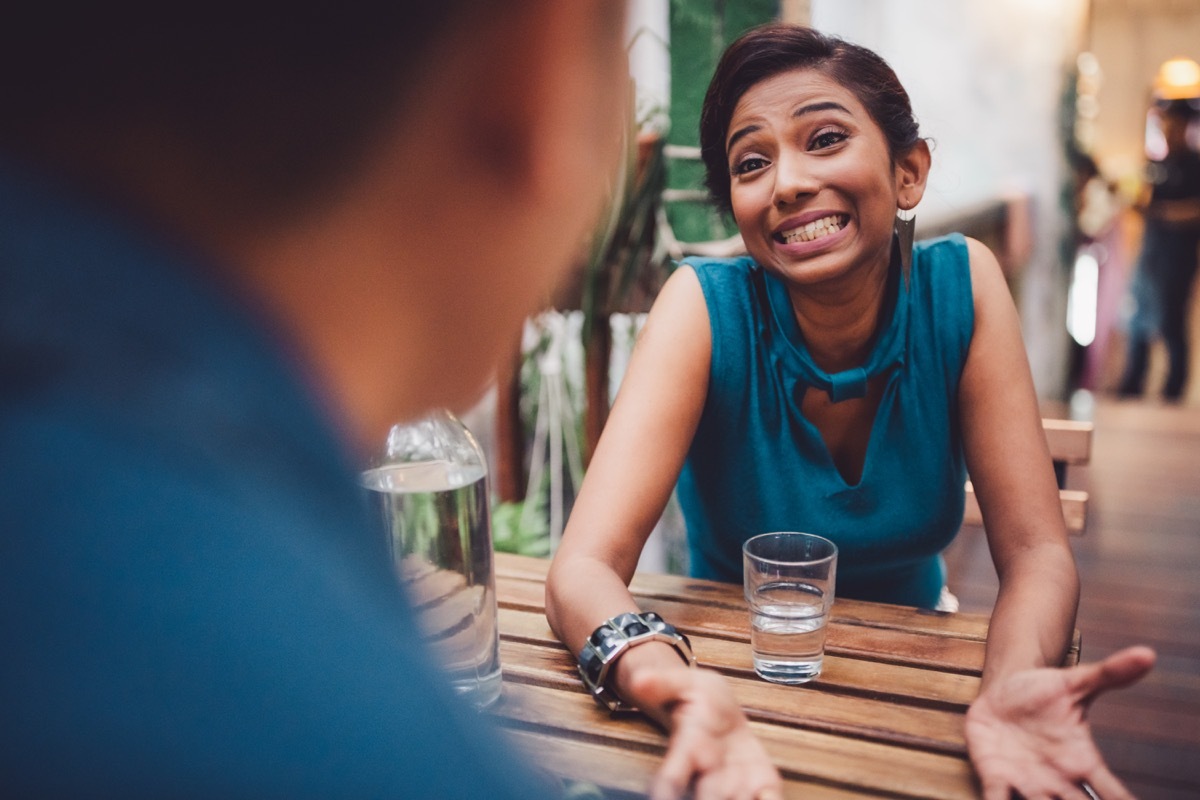 Young woman sitting in stylish cafe apologizing, gesturing and searching for an excuse to tell her boyfriend