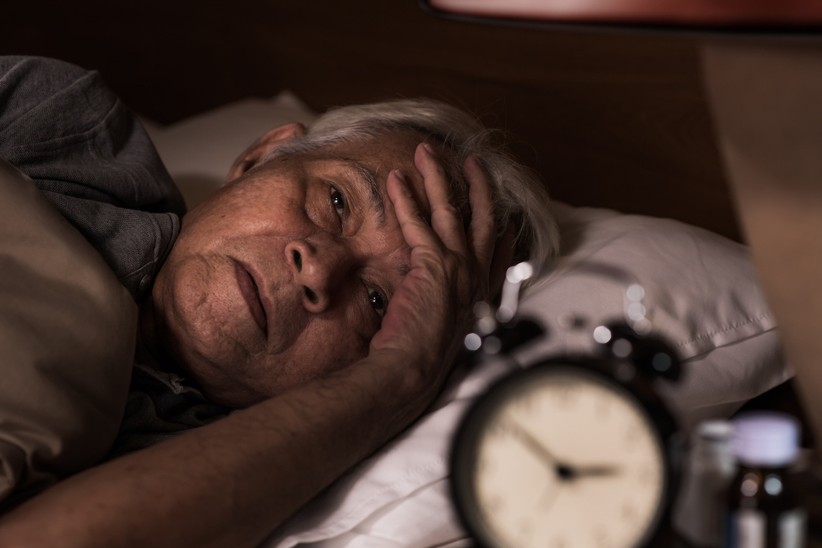 Asian senior man lying in bed but cannot sleep from insomnia