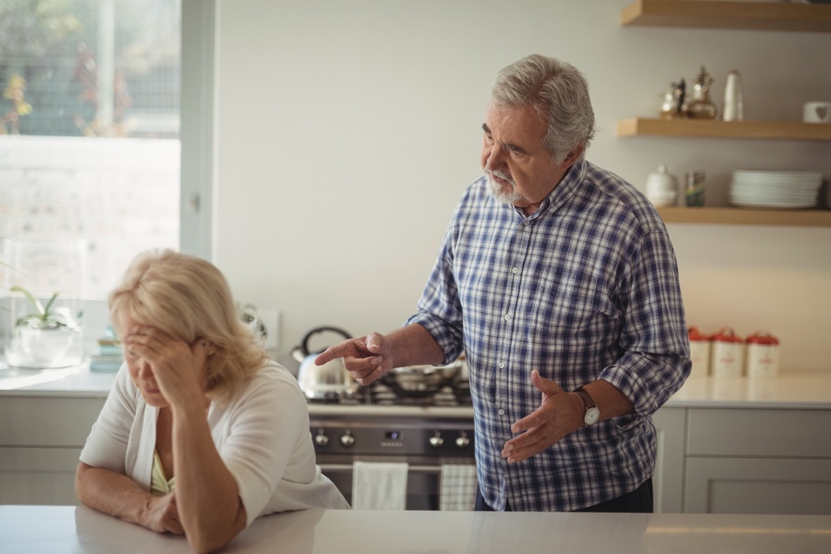 Senior couple arguing in kitchen at home, woman leans on island with head in hands