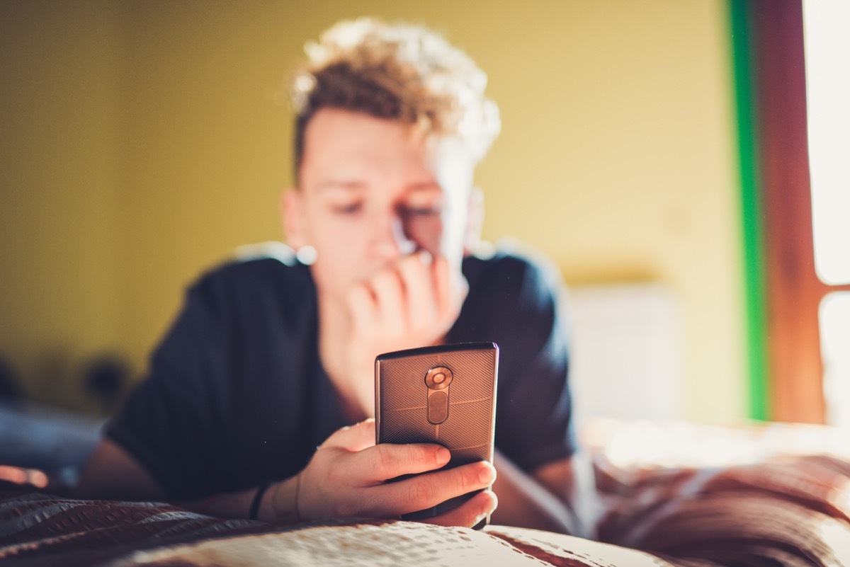 Teenage Boy Using his Smart Phone while Laying on the Bed