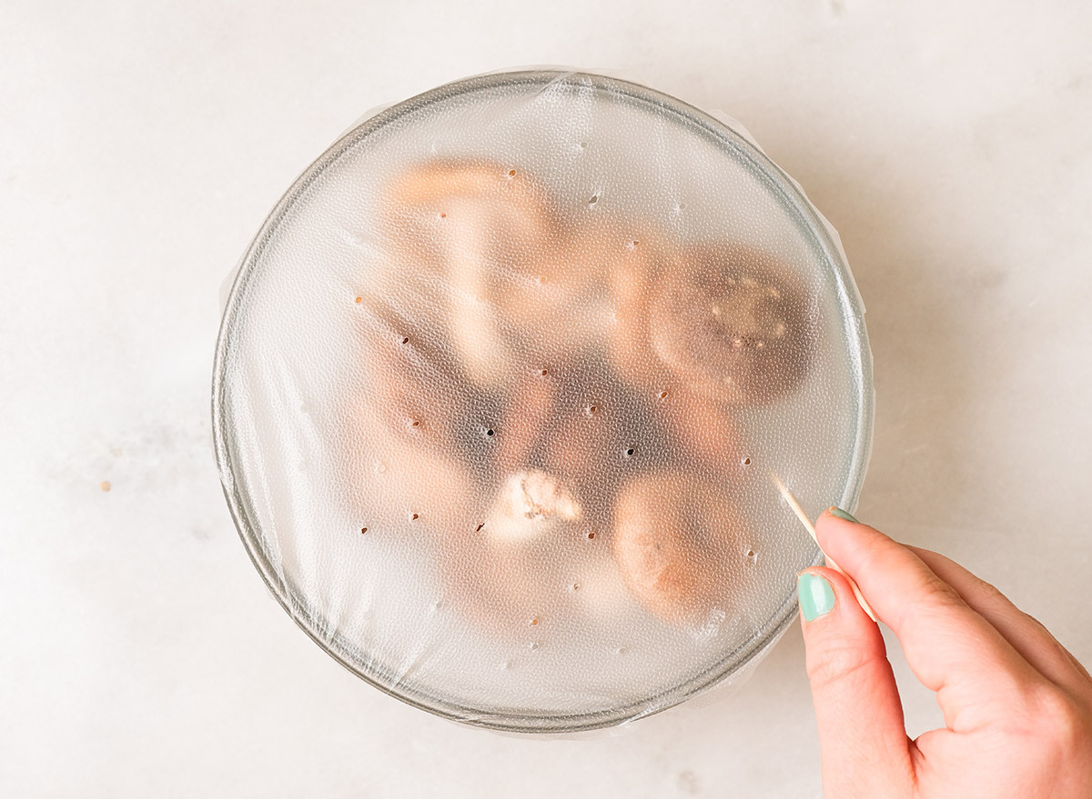 poking holes into plastic wrap covering a bowl of mushrooms