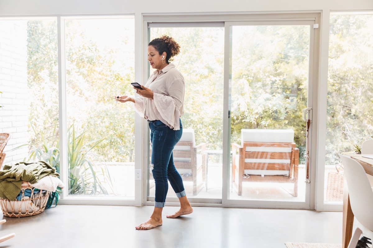 Wearing casual clothes and walking barefoot at home, the mid adult business woman joins colleagues for a video conference.