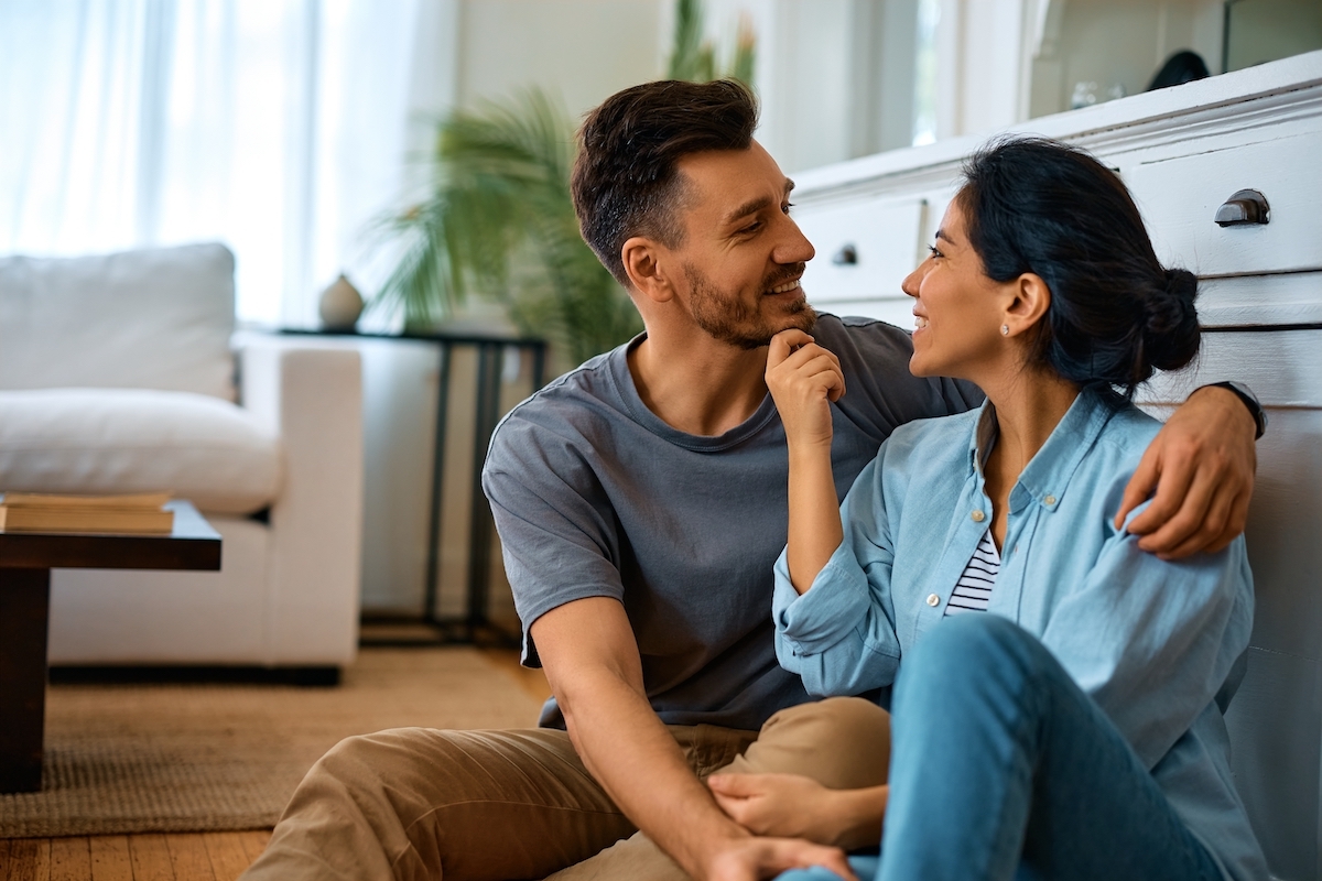 A happy couple sitting on the living room floor and talking.