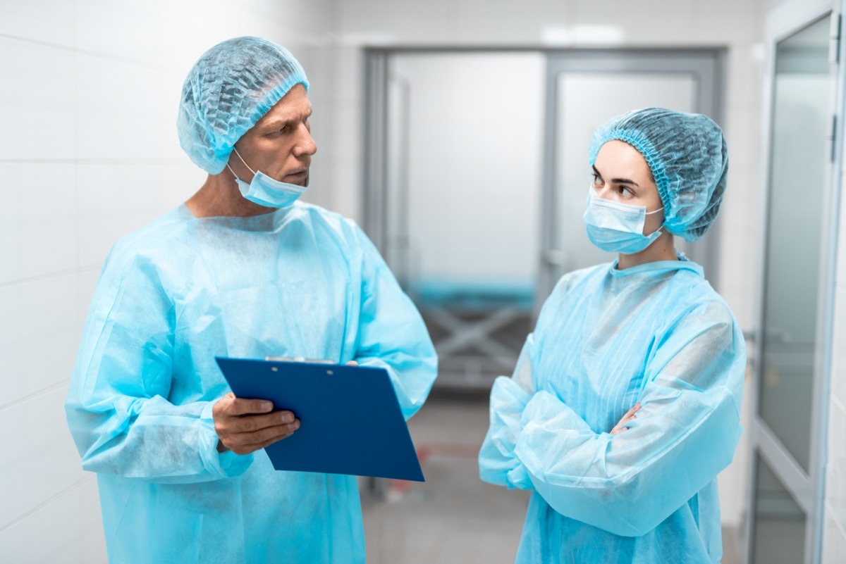 Two professional doctors in blue medical uniform standing in front of each other in hospital corridor and looking thoughtful