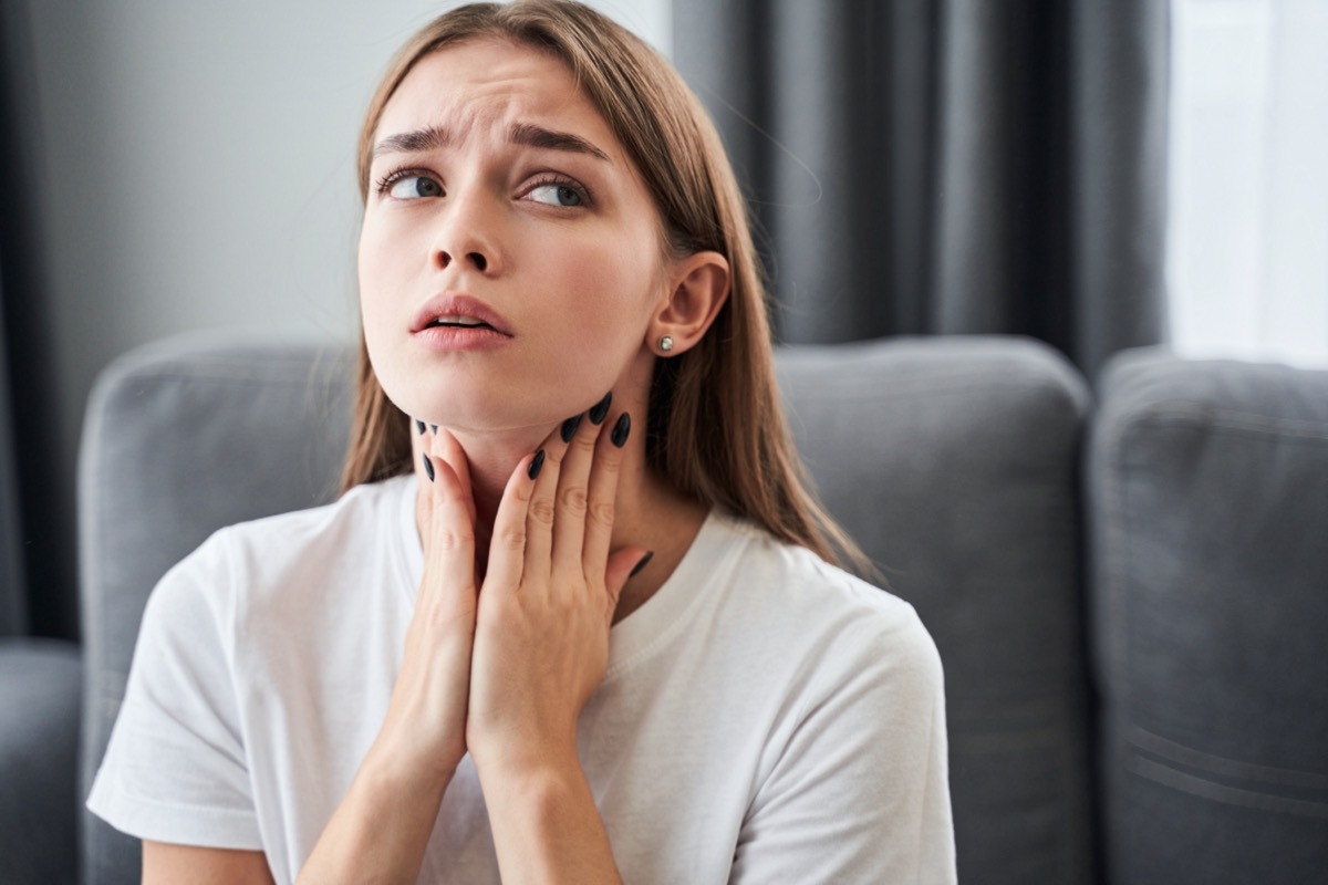 woman touching her neck and feeling pain in throat while sitting in the living room at home.