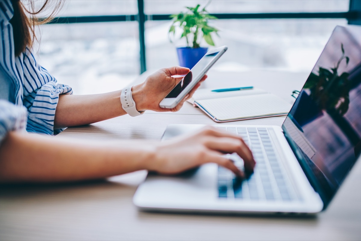 cropped image of a woman at work on her computer while receiving a text on her phone