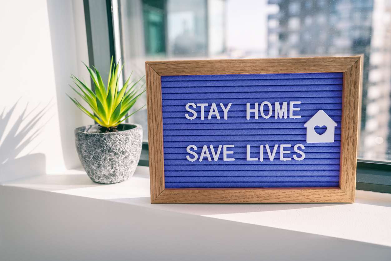 A blue sign on a windowsill that says stay home save lives