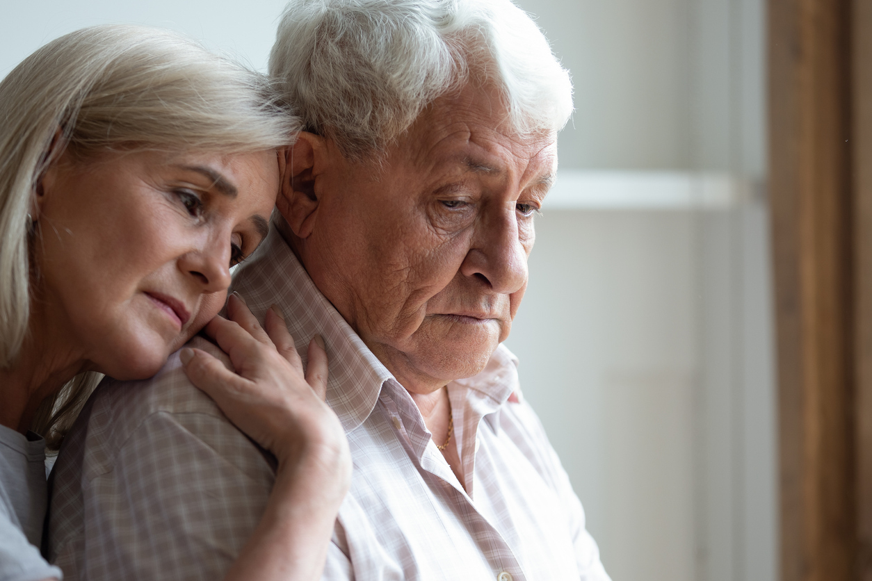 A middle-aged woman hugging an older man suffering from dementia