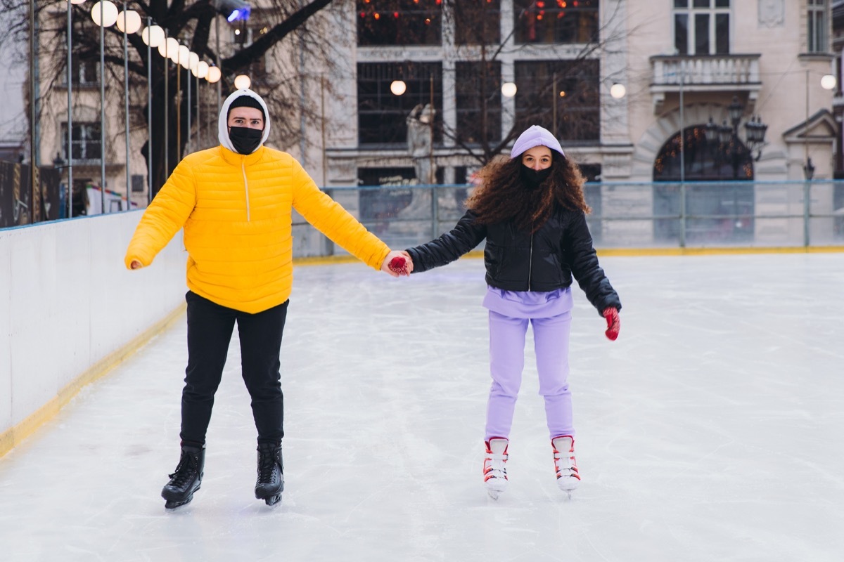 Young couple in face masks enjoying the wonderful winter day ice skating outdoors in the city centre