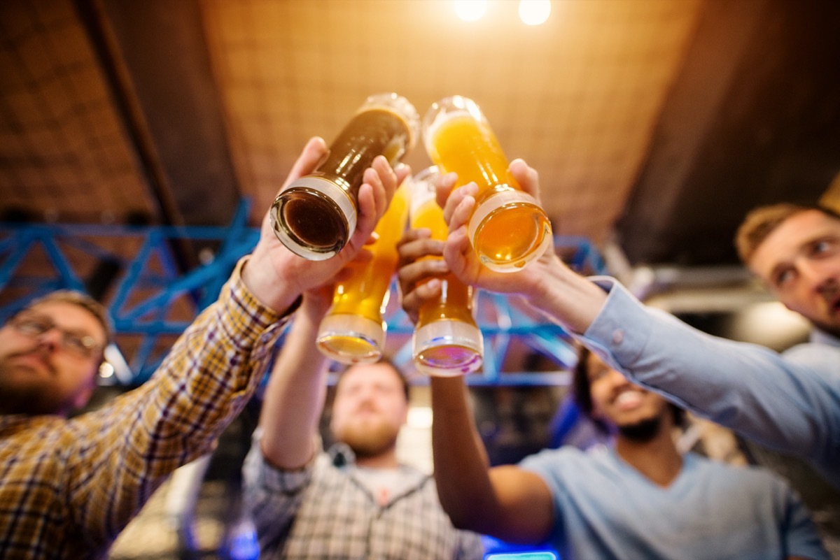 close up from below of four beers being toasted by young men