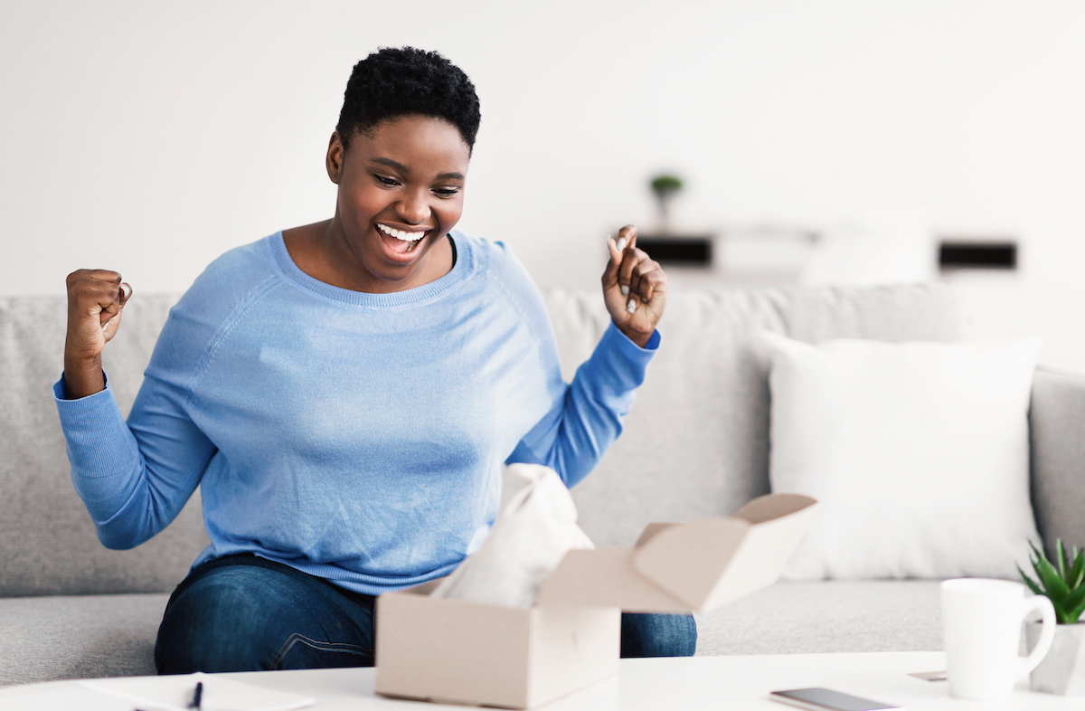 An excited woman sitting on her couch opening a package