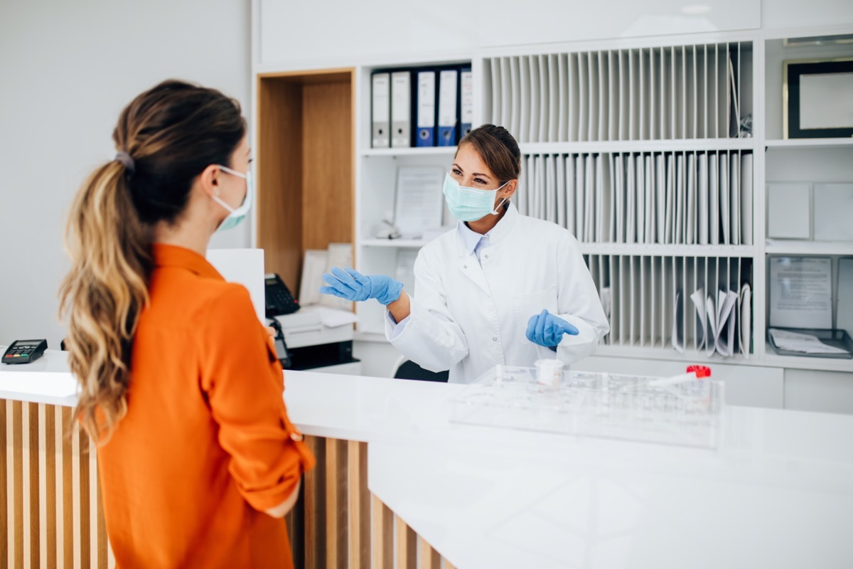 female practitioner or nurse with face protective mask working at clinic reception desk