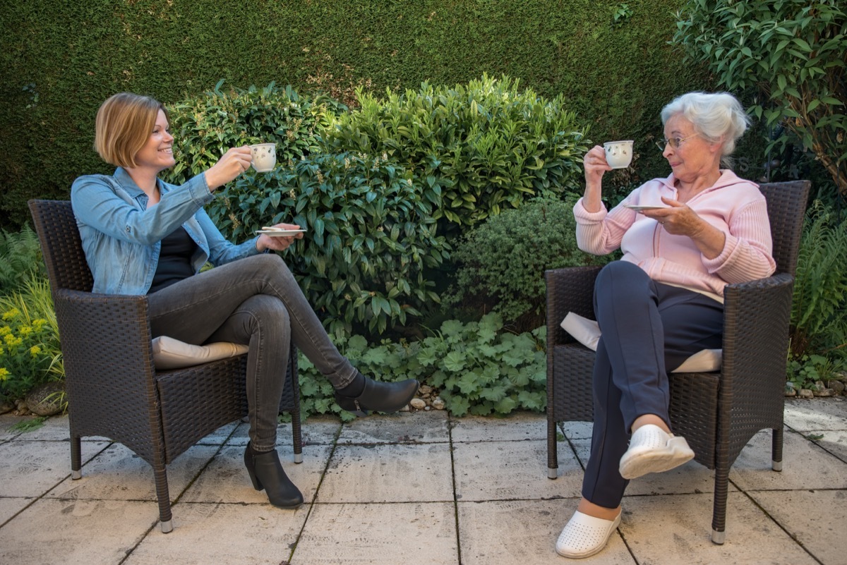 Senior woman and daughter with face masks having coffee with safety distance