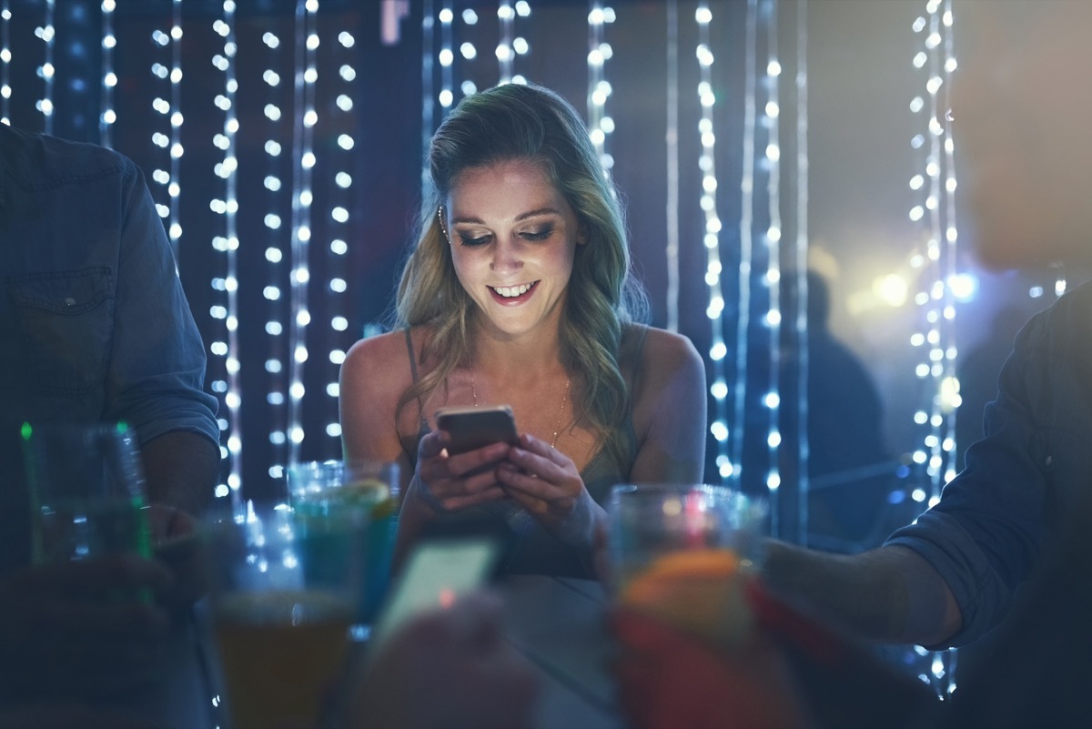 shot of a young woman texting on her smartphone while sitting in a crowded nightclub