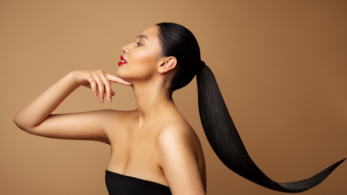 Beauty Model Profile. Young Woman with long Ponytail Hair. Women Face Side view over beige background. Lady with Red Lipstick and Black Straight Tail Hairstyle