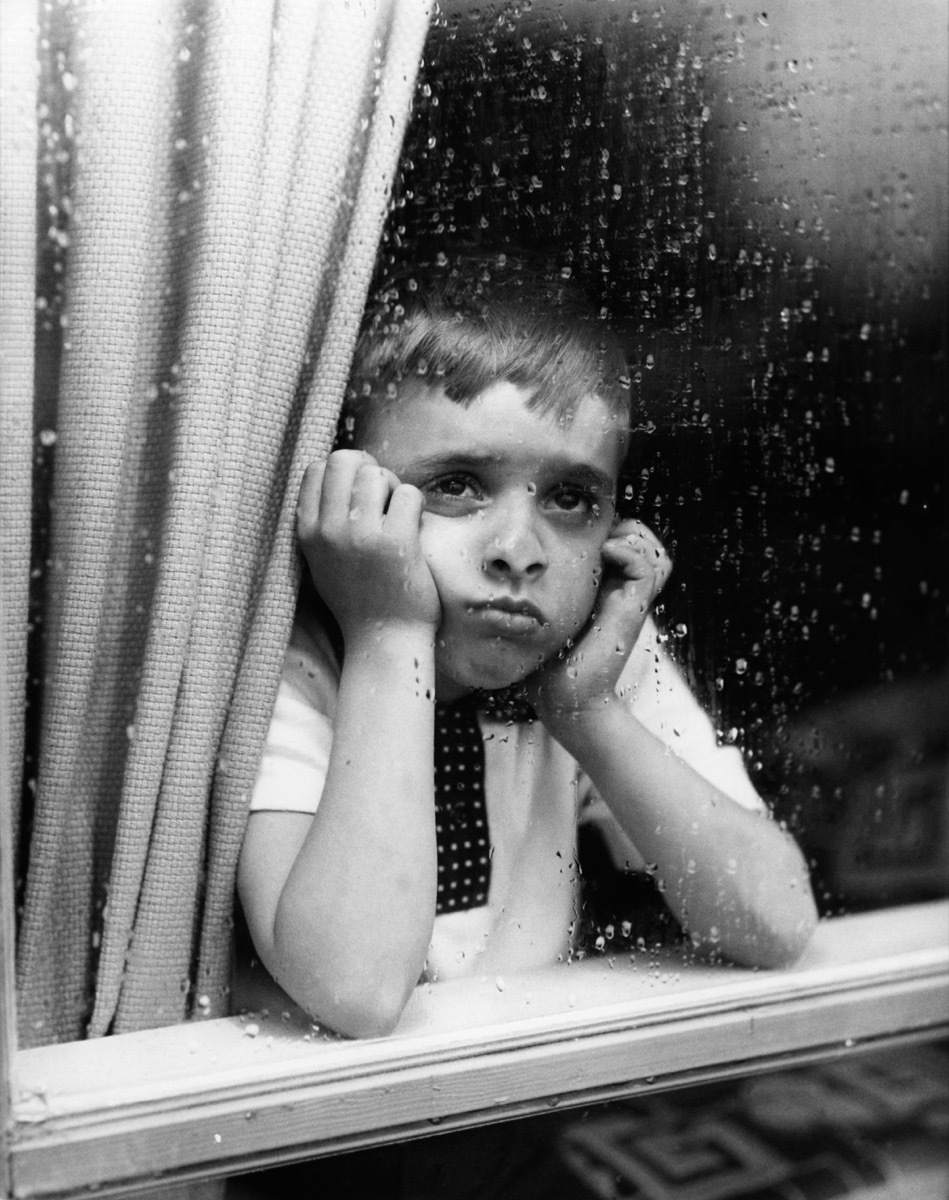 1950s sad boy looks out window with hands on chin, shows how different parenting was in the 1950s