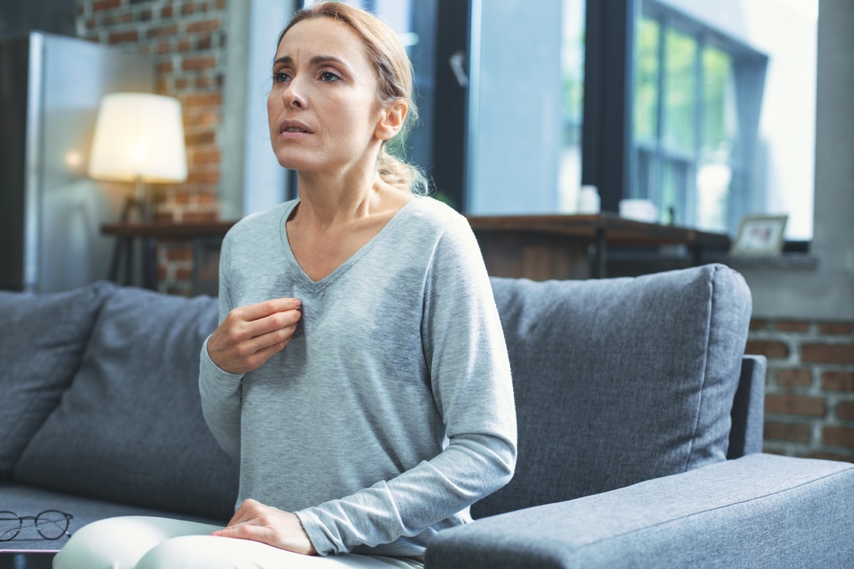 Hot flashes. Exhausted mature woman resting on sofa and having hot flash