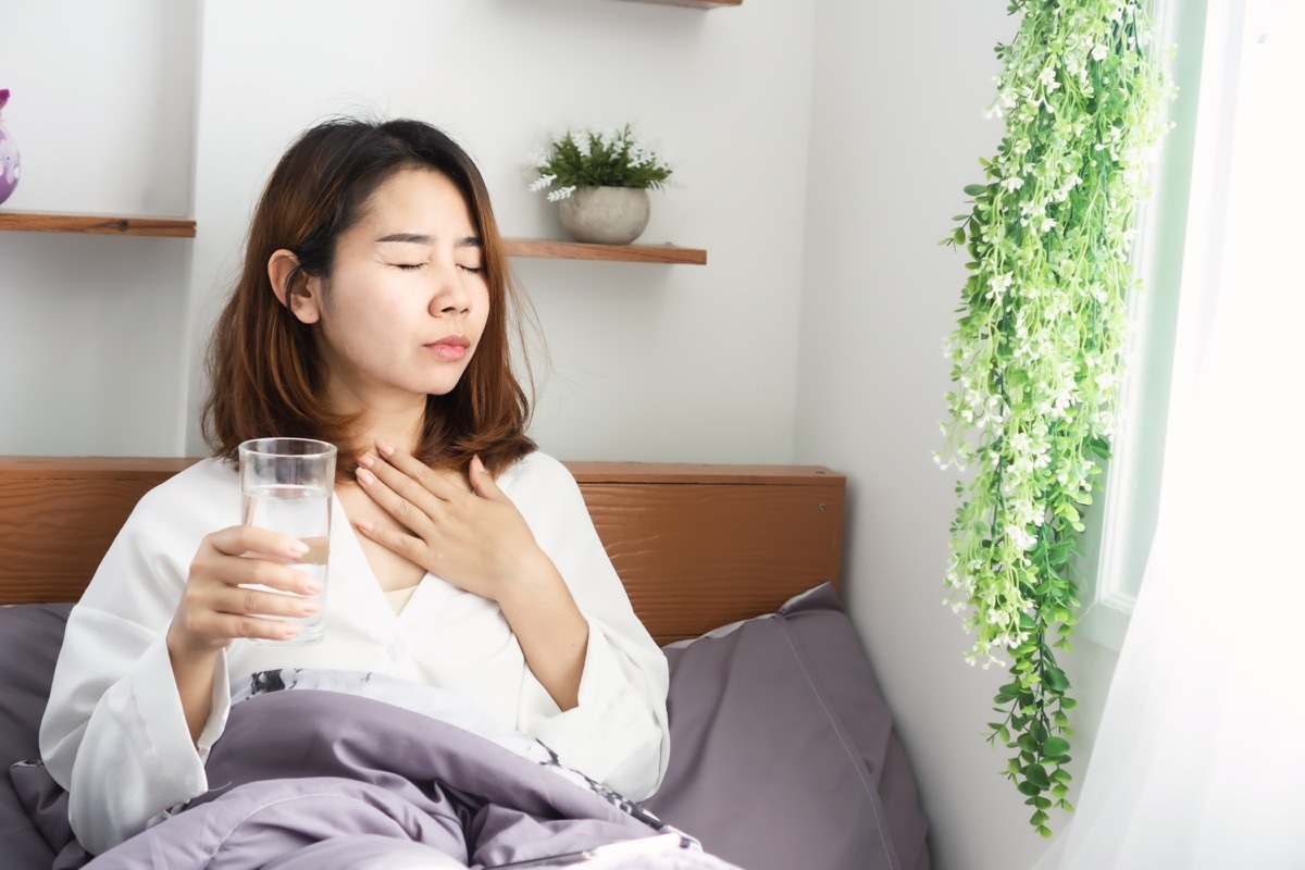 woman suffering from sore throat drinking water in her bed