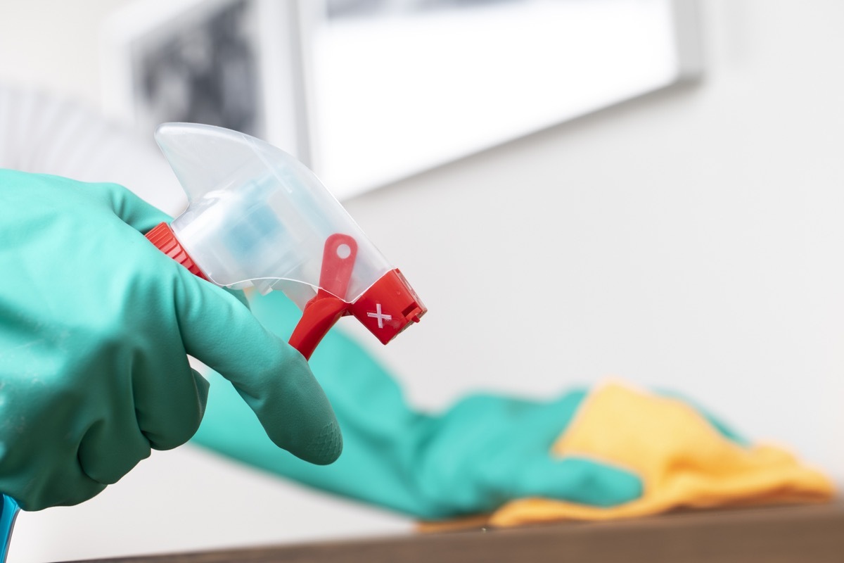 Woman in rubber gloves using spray cleaner on counter, close up.