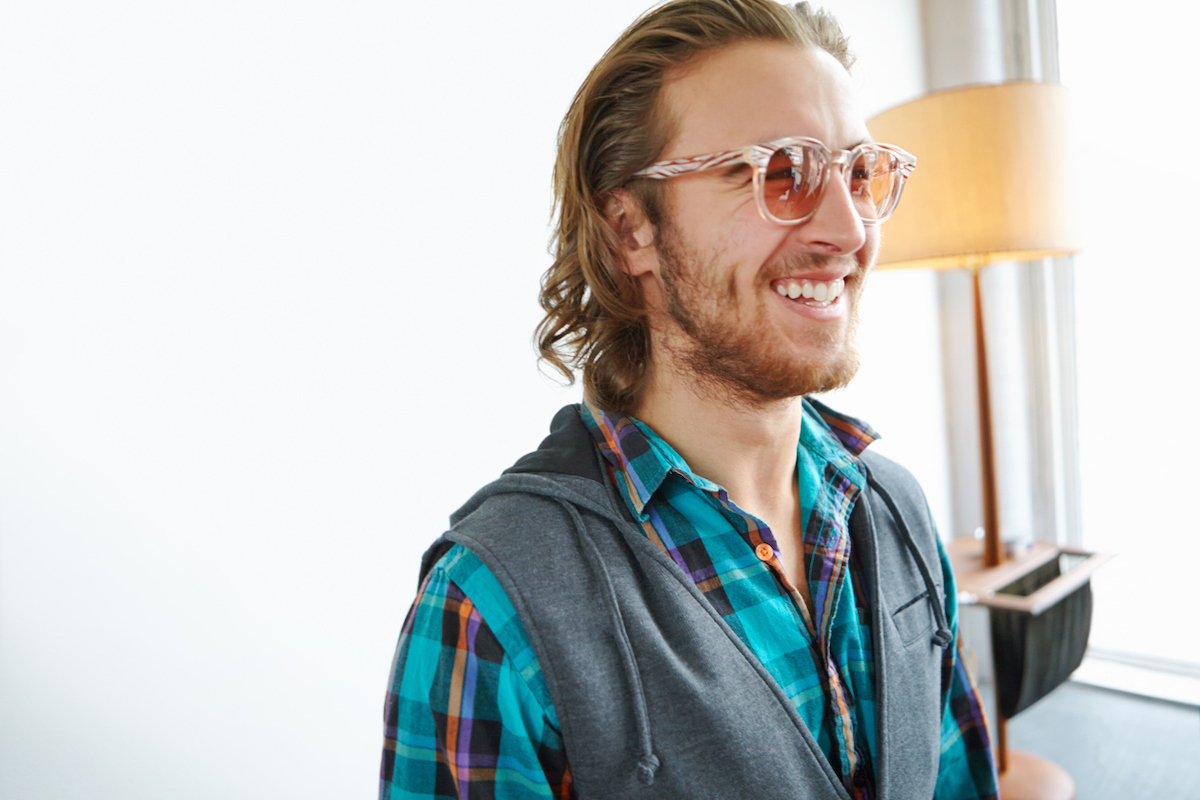 Portrait of a smiling young man wearing a plaid shirt, sweatshirt vest, and large glasses