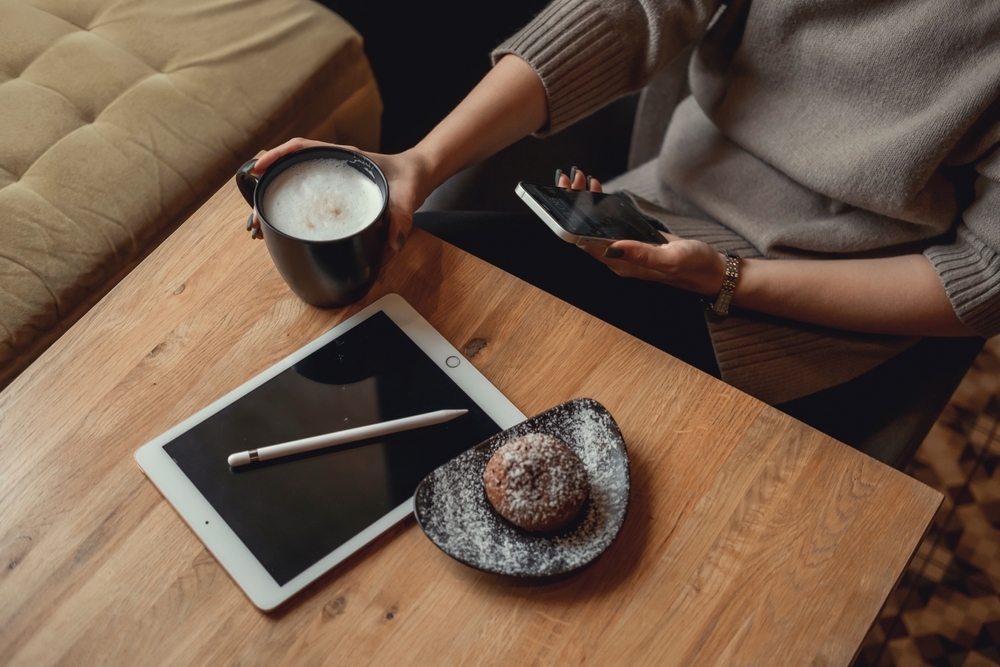 A woman sitting in a cafe using an iPhone and iPad while drinking coffee