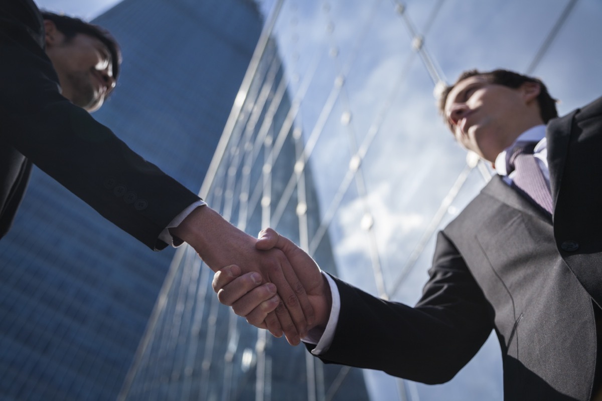 two business men shaking hands in front of a skyscrapper